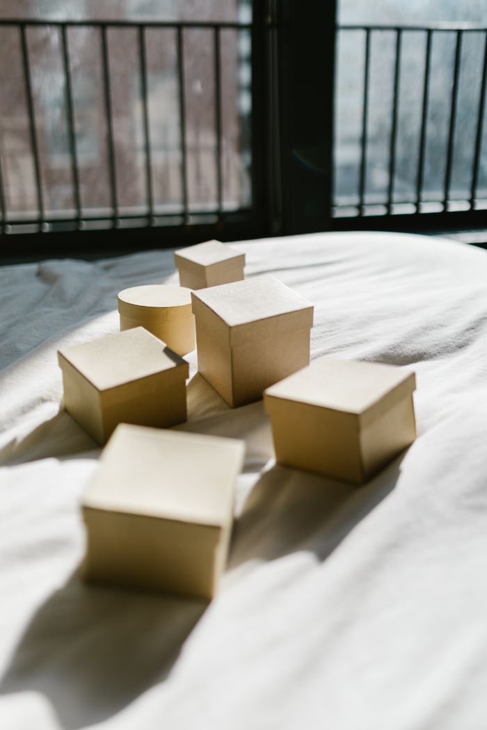 Sunlit assortments of boxes on a bed with city view in the background, casting intriguing shadows.